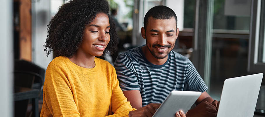 smiling couple using a laptop and mobile tablet to house hunt online